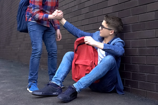 student reaching out and offering their hand to help another student stand up after being bullied